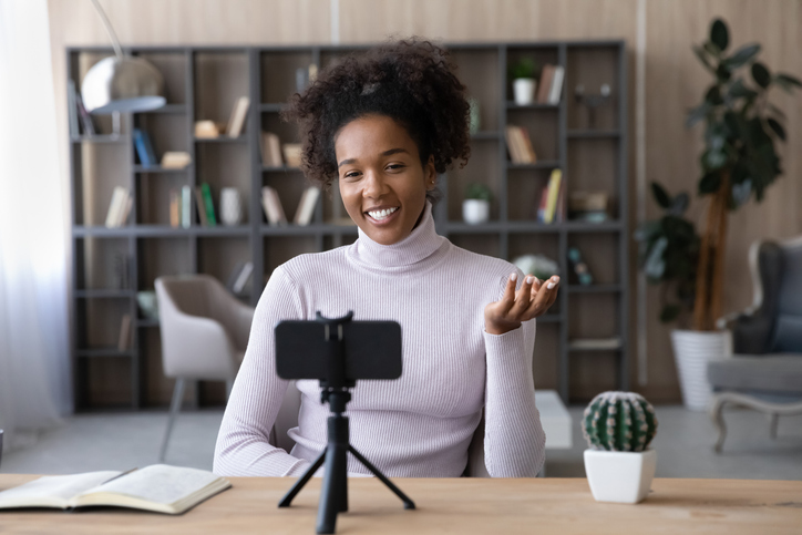 Smiling African American woman recording video on smartphone at workplace